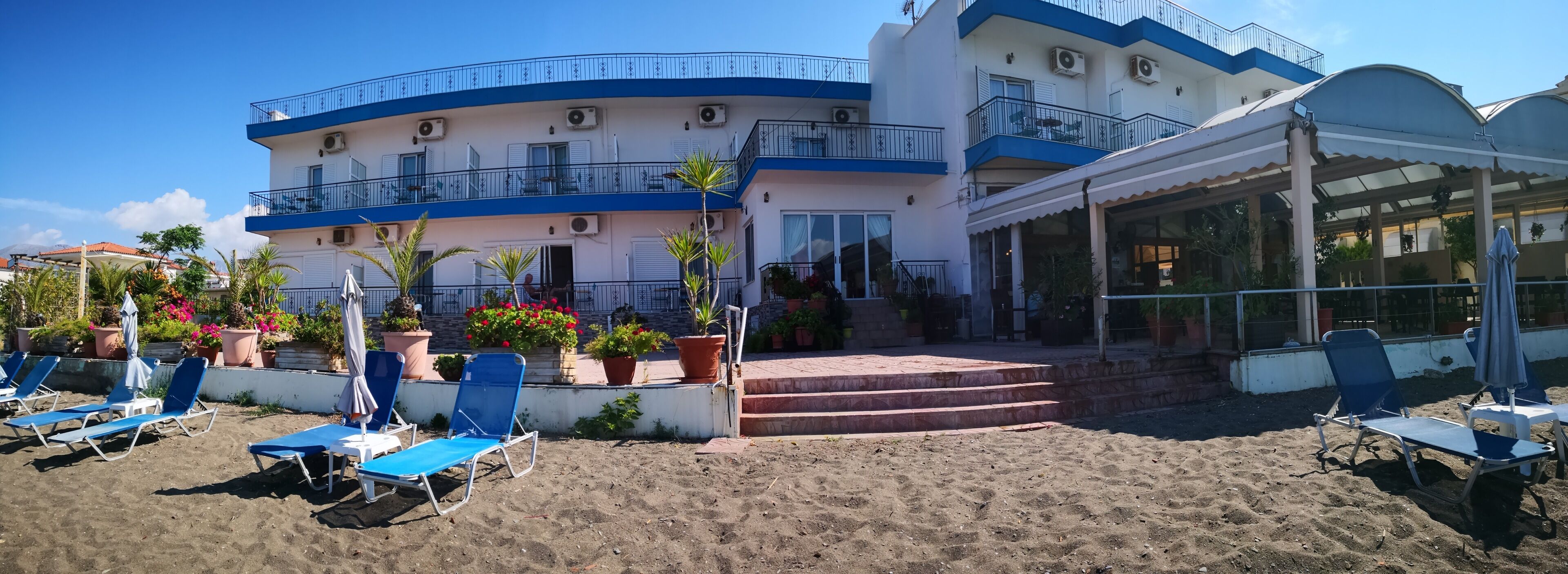 A beachfront hotel with blue and white exterior, outdoor seating, and a covered patio area.