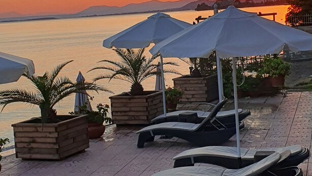 Una terraza con sillones de descanso y sombrillas frente a una masa de agua al atardecer.