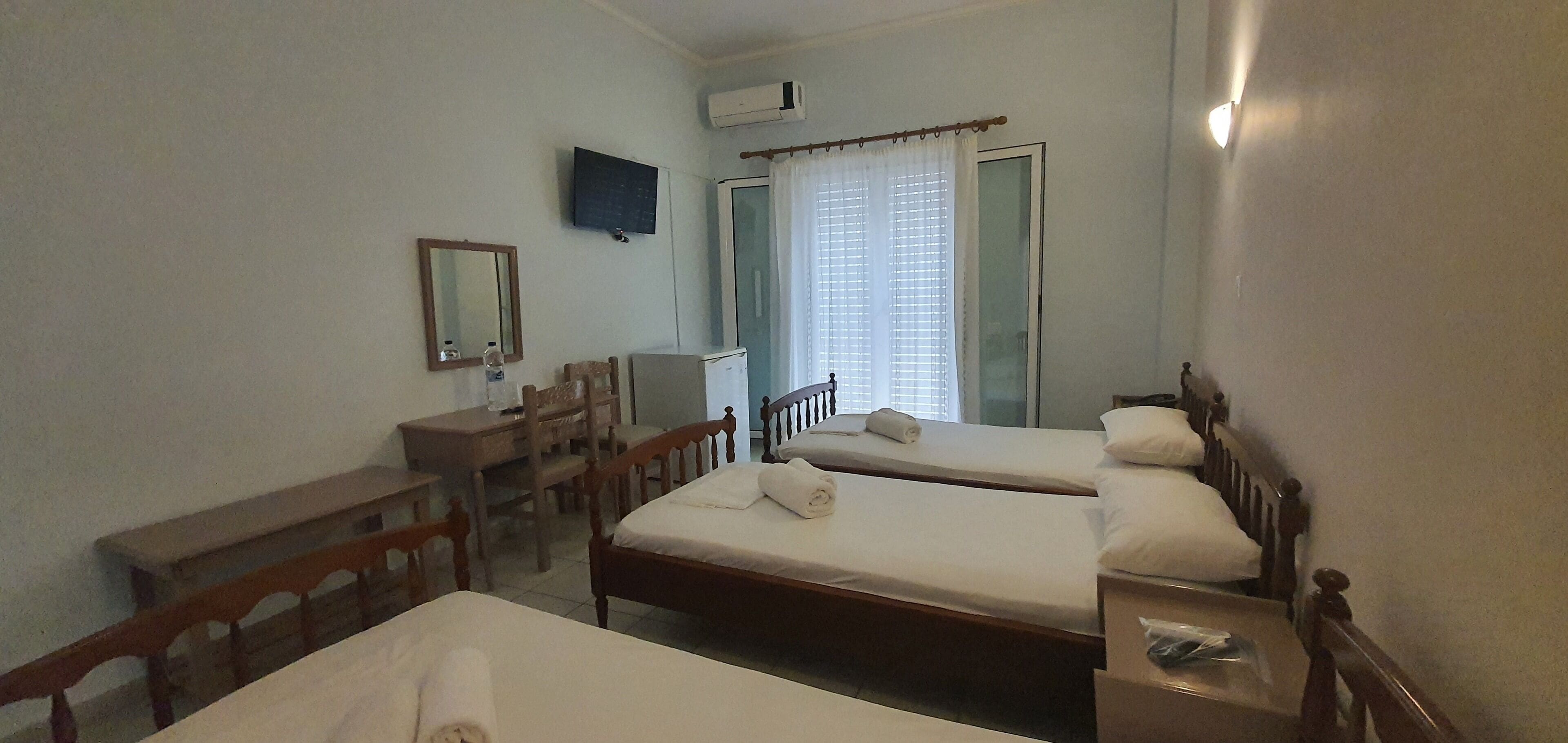 A hotel room with two beds, a desk, a chair, a TV, and a window with curtains.