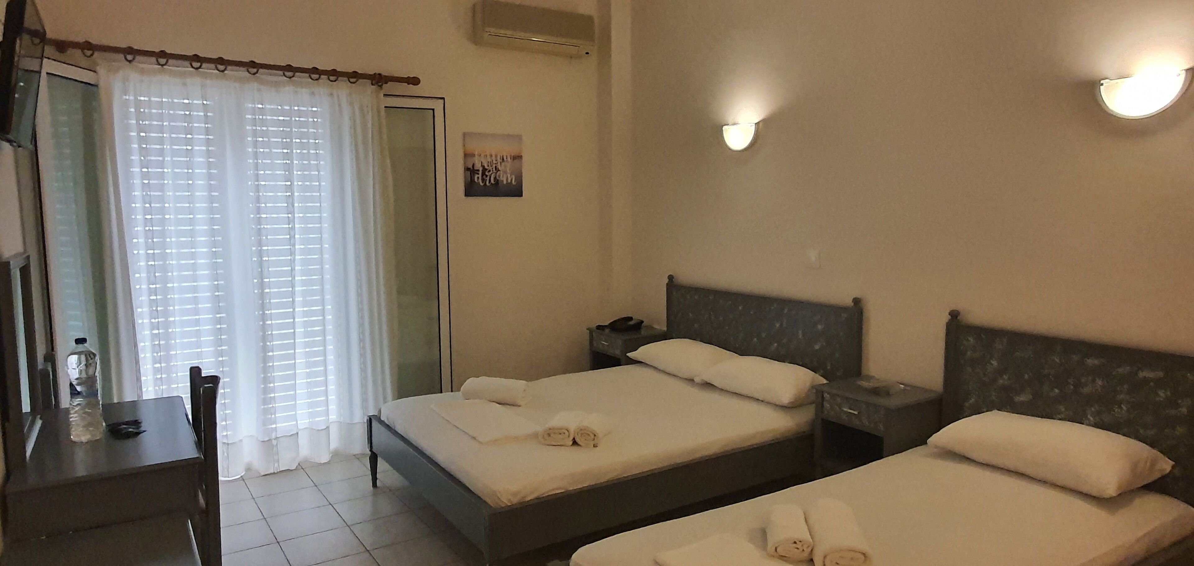 Une chambre d’hôtel avec deux lits, un bureau, une chaise, une fenêtre avec des rideaux et un luminaire fixé au mur.