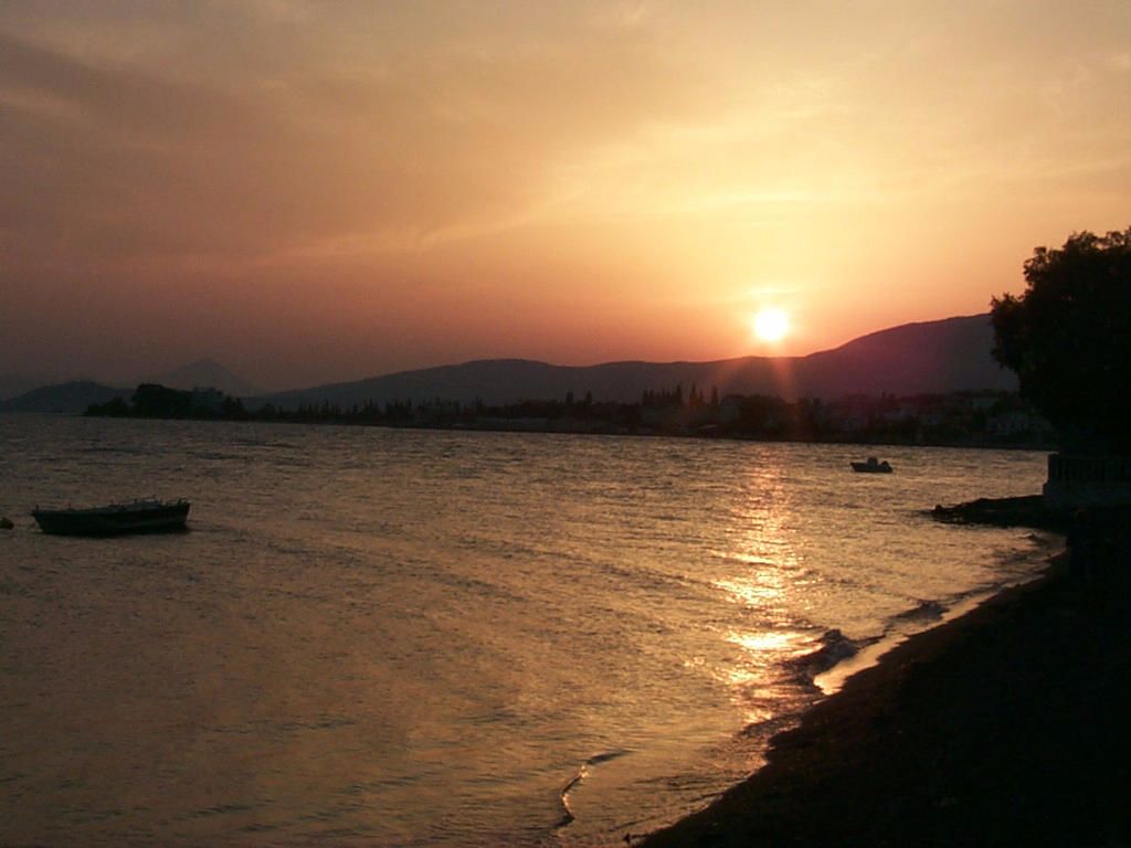 Um pôr do sol sobre a água, com barcos e uma costa distante.