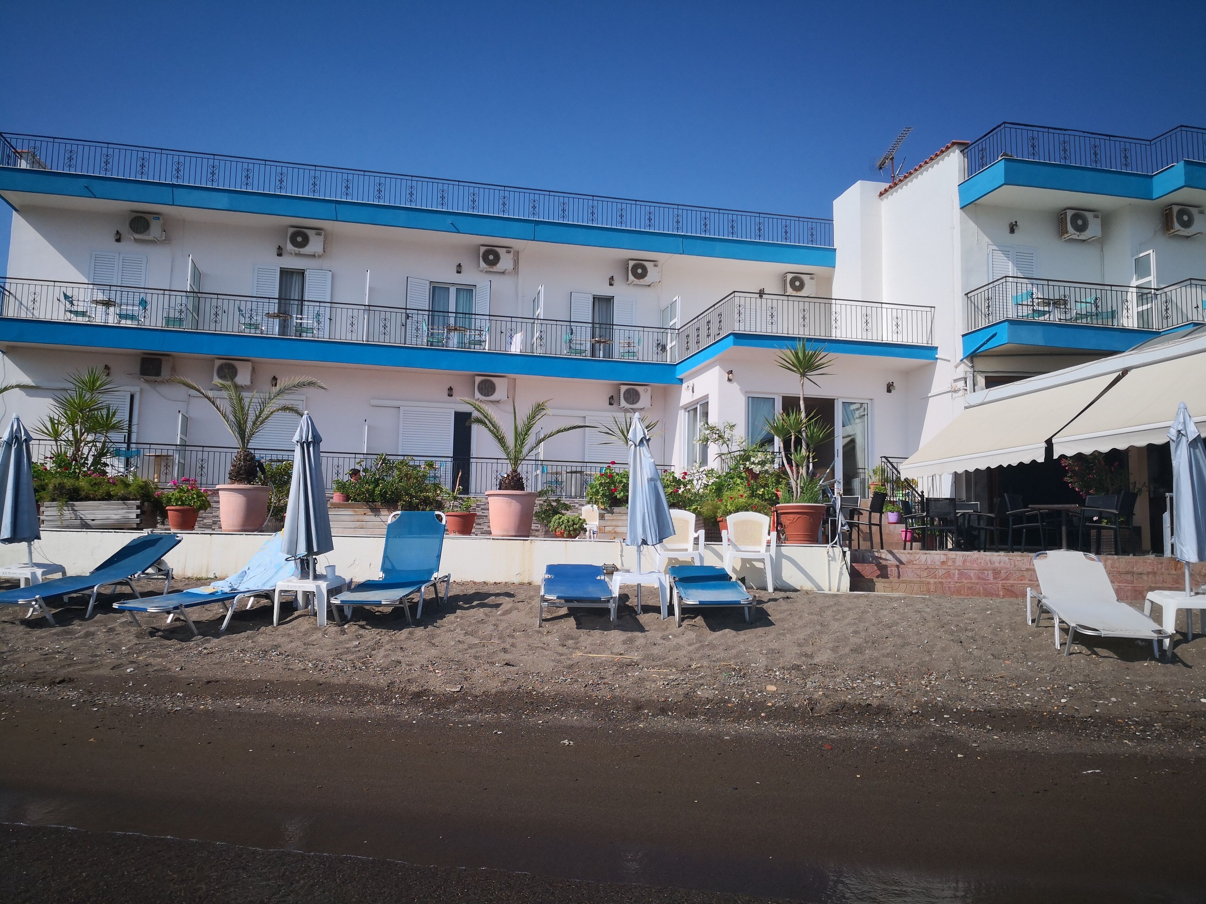 A beachfront hotel with multiple balconies, outdoor seating, and potted plants.