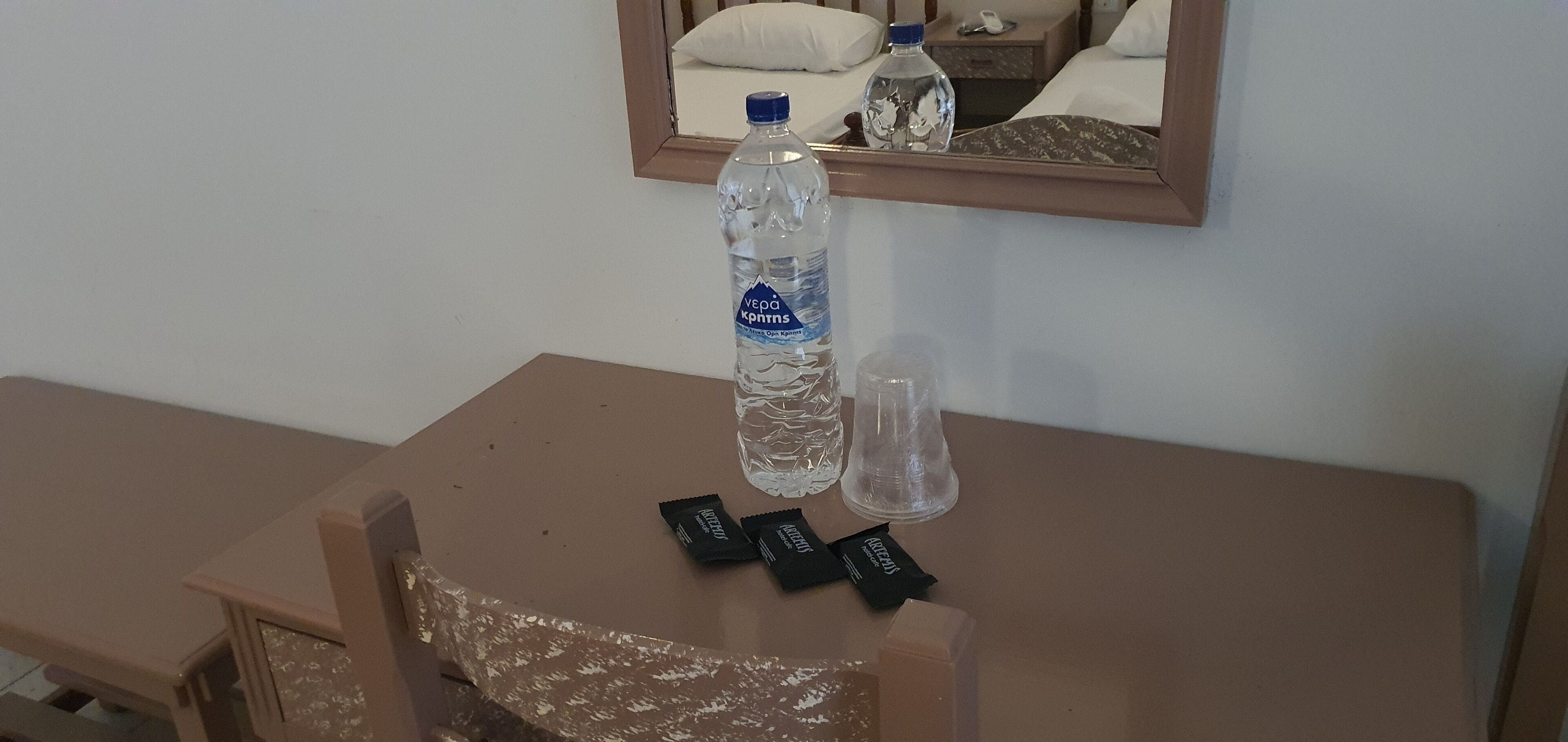 Una pequeña mesa con una botella de agua, una botella de vidrio y dos paquetes de chocolate.