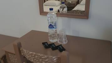 Een klein tafeltje met een waterfles, een glazen fles en twee pakjes chocolade.