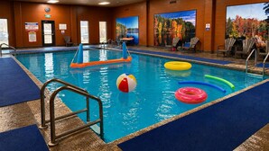 An indoor swimming pool with a lifeguard station, poolside chairs, and a mural of autumn foliage.