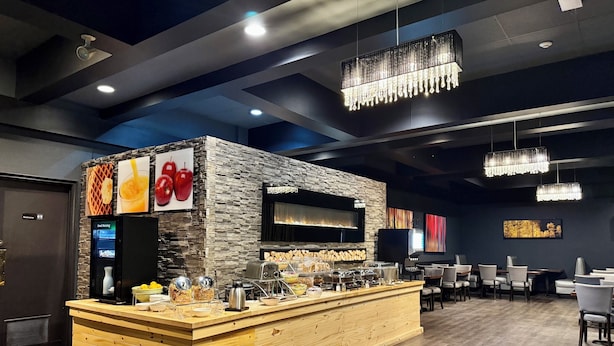 A breakfast bar with a stone wall backdrop, a digital clock, and various breakfast items. - Quality Inn Fort Frances (Fort Frances)