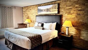A hotel room with a large bed, two bedside tables with lamps, a headboard with a painting, and a brick-patterned wall.