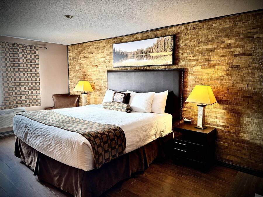 A hotel room with a large bed, two bedside tables with lamps, a headboard with a painting, and a brick-patterned wall.