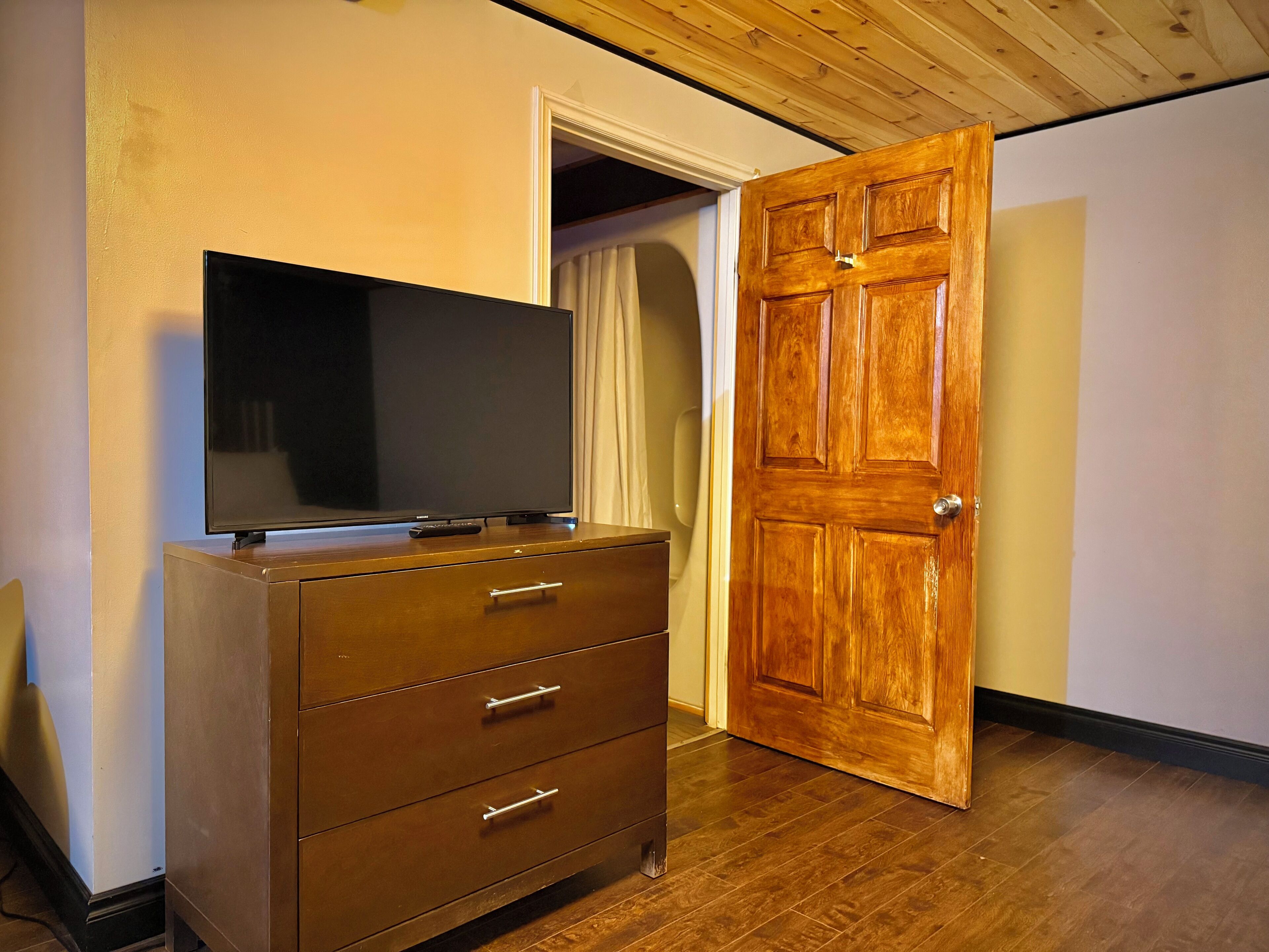 Un aparador de madera con un televisor de pantalla plana encima, una puerta de madera y un techo de madera.