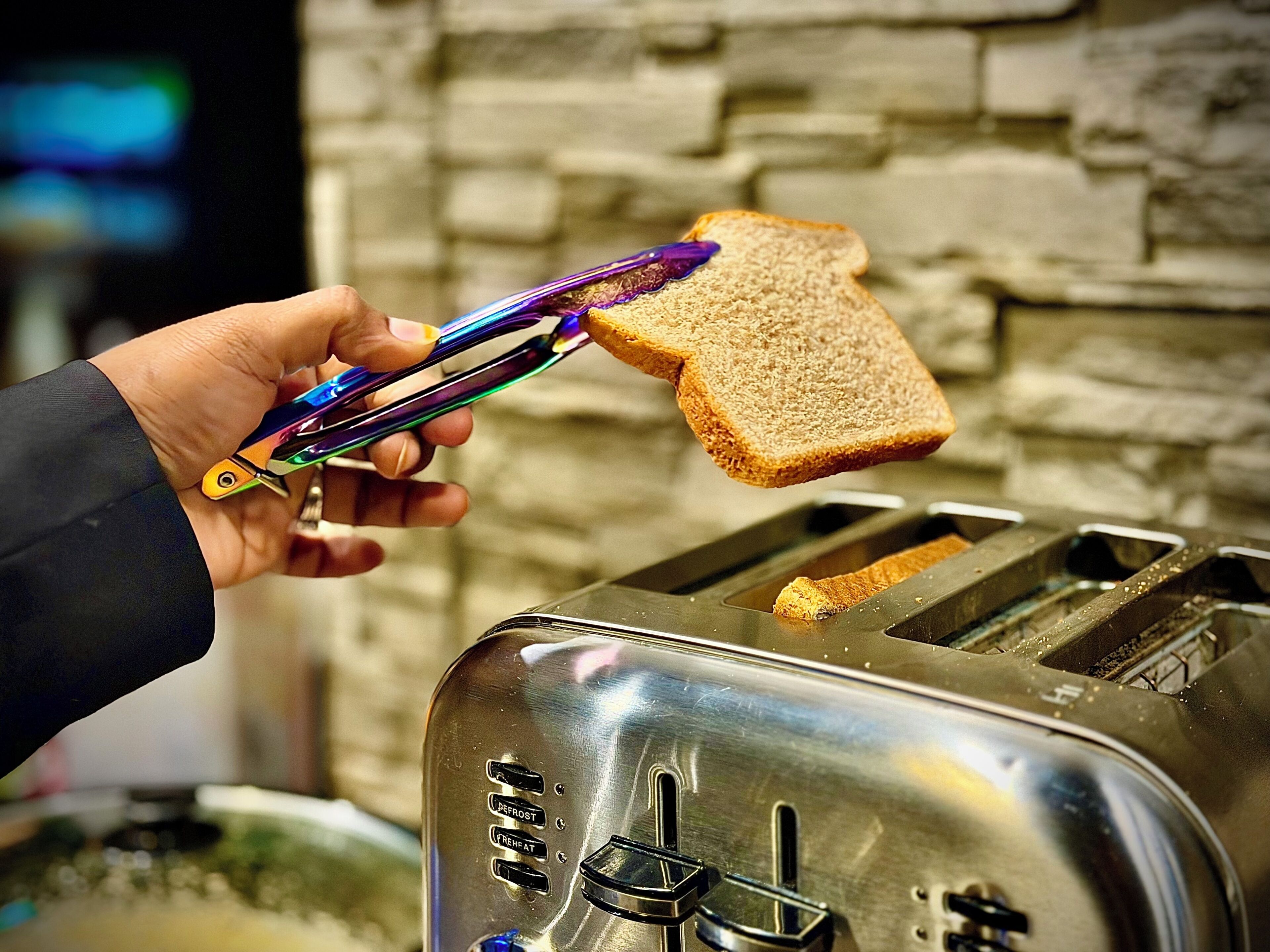Una mano sosteniendo unas tijeras con un trozo de pan sobre una tostadora.