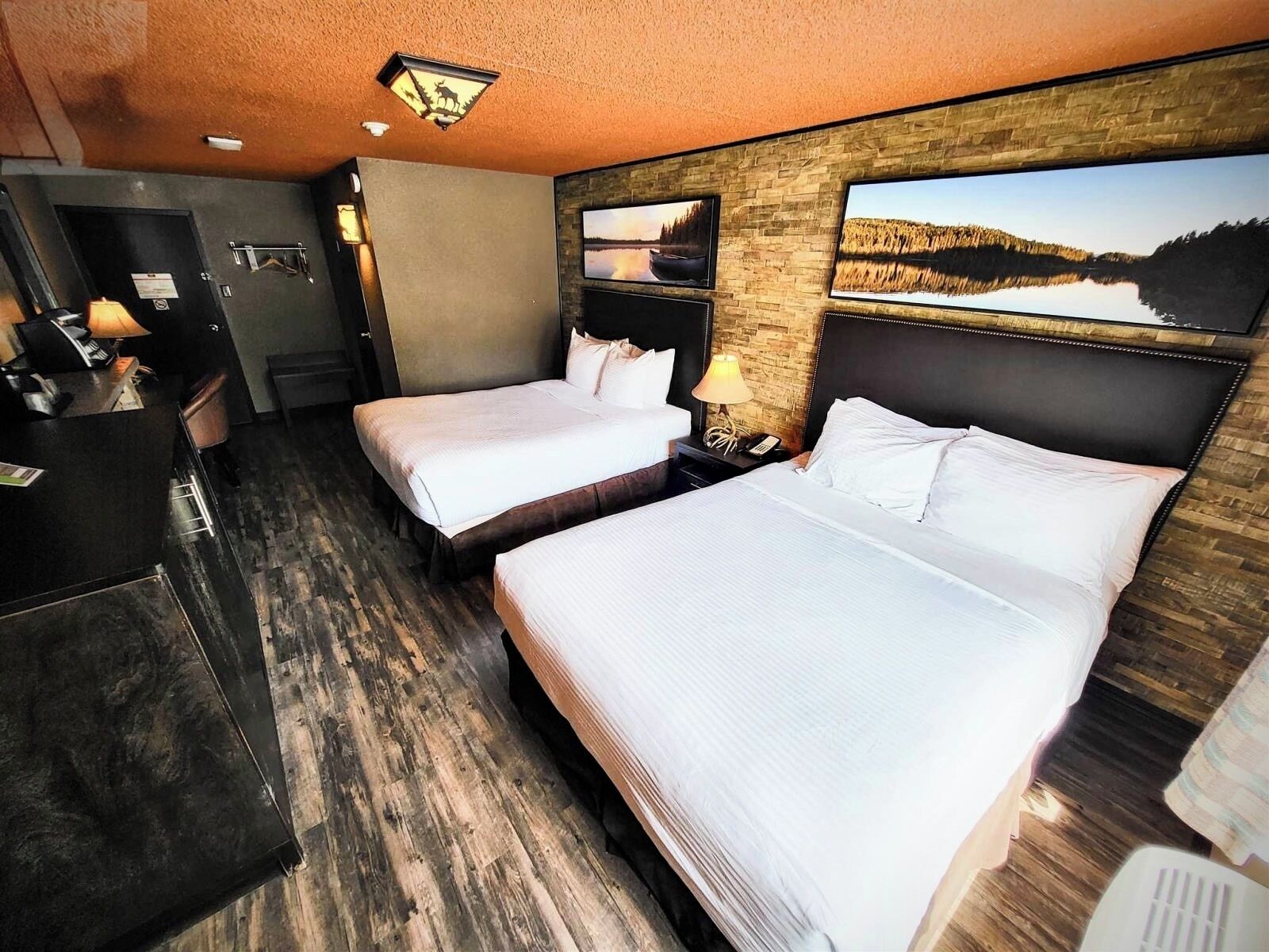 A hotel room with two beds, a desk, a chair, a lamp, and a wall-mounted TV.