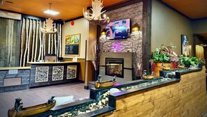 A lobby with a reception desk, a stone fireplace, a television mounted on the wall, and a decorative water feature. - Quality Inn Fort Frances (Fort Frances)