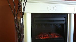 A fireplace with a white mantel and a glass door, displaying a fire inside. - The Walla Walla Inn (Rainy River)
