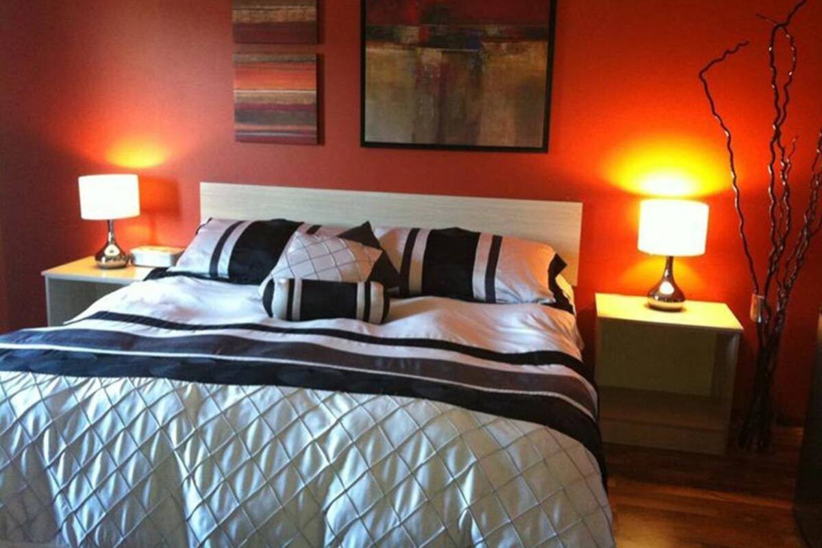 A neatly made bed with a striped pillow and a quilted duvet, two bedside lamps, and a wall with abstract art.