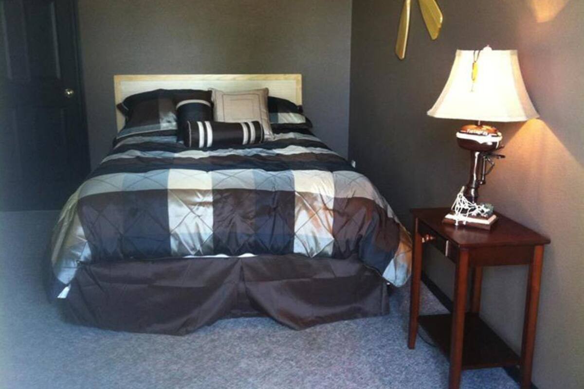 A bedroom with a bed, a bedside table with a lamp, and a door.