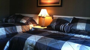 A hotel room with two beds, a nightstand, a lamp, and a painting on the wall. - The Walla Walla Inn (Rainy River)