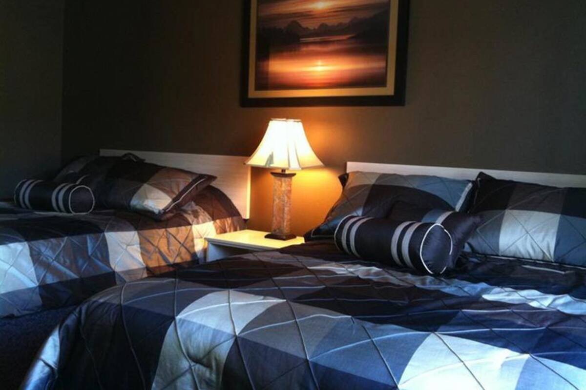 A hotel room with two beds, a nightstand, a lamp, and a painting on the wall.