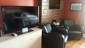 A room with a large flat-screen TV on a wooden cabinet, two black leather sofas, a small table with salt and pepper shakers, and a window with blinds. - The Walla Walla Inn (Rainy River)