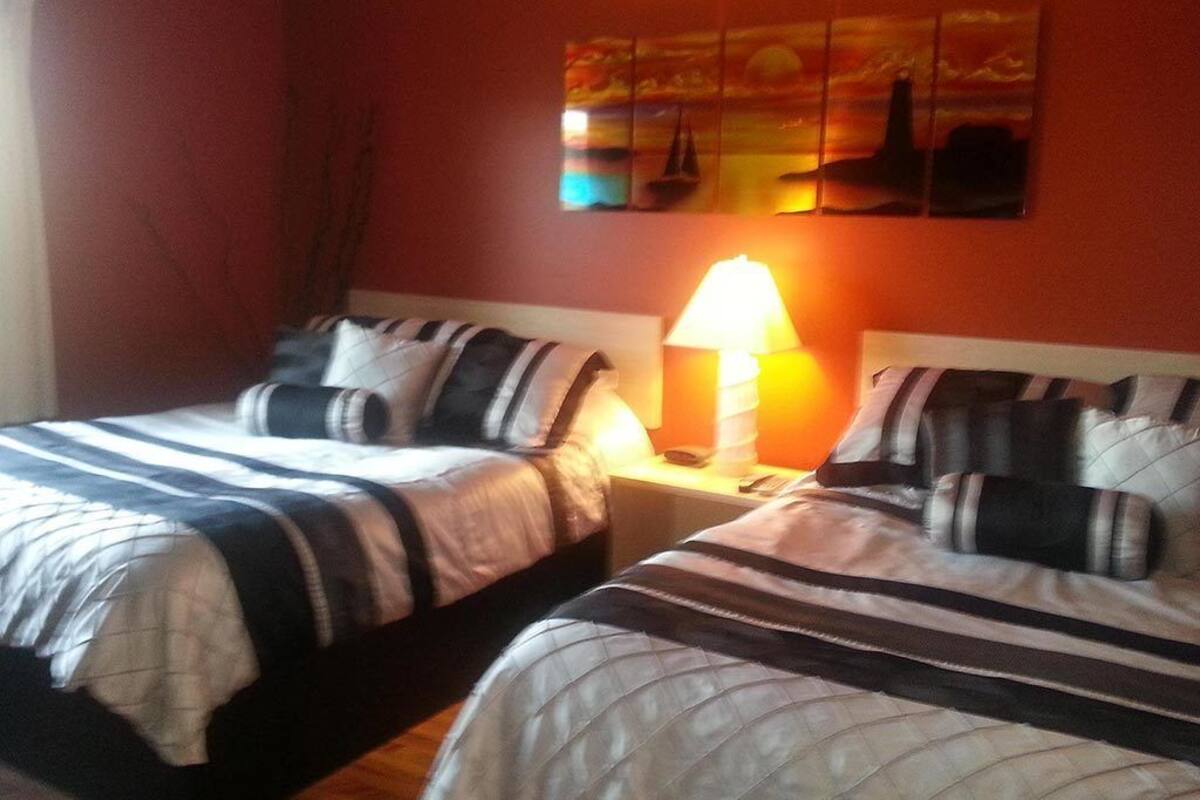 A room with two beds, each with striped bedding and pillows, a nightstand with a lamp, and a wall painting above the beds.