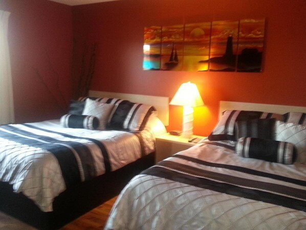 Una habitación con dos camas, cada una con ropa de cama y almohadas a rayas, una mesita de noche con lámpara, y un cuadro en la pared sobre las camas.