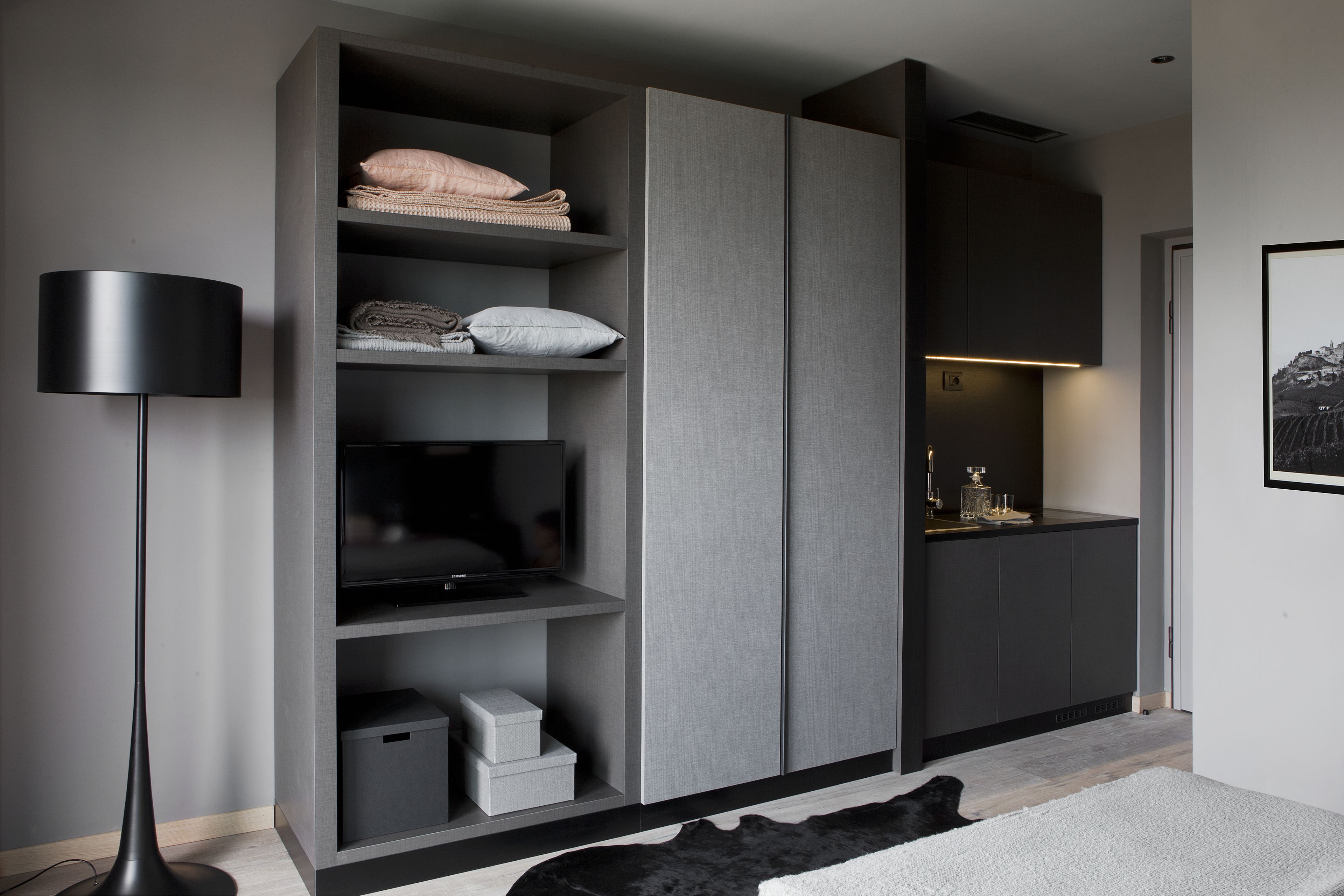 Un salon moderne doté d’un meuble de rangement intégré pour les appareils multimédias, d’un lampadaire et d’un tapis noir et blanc.