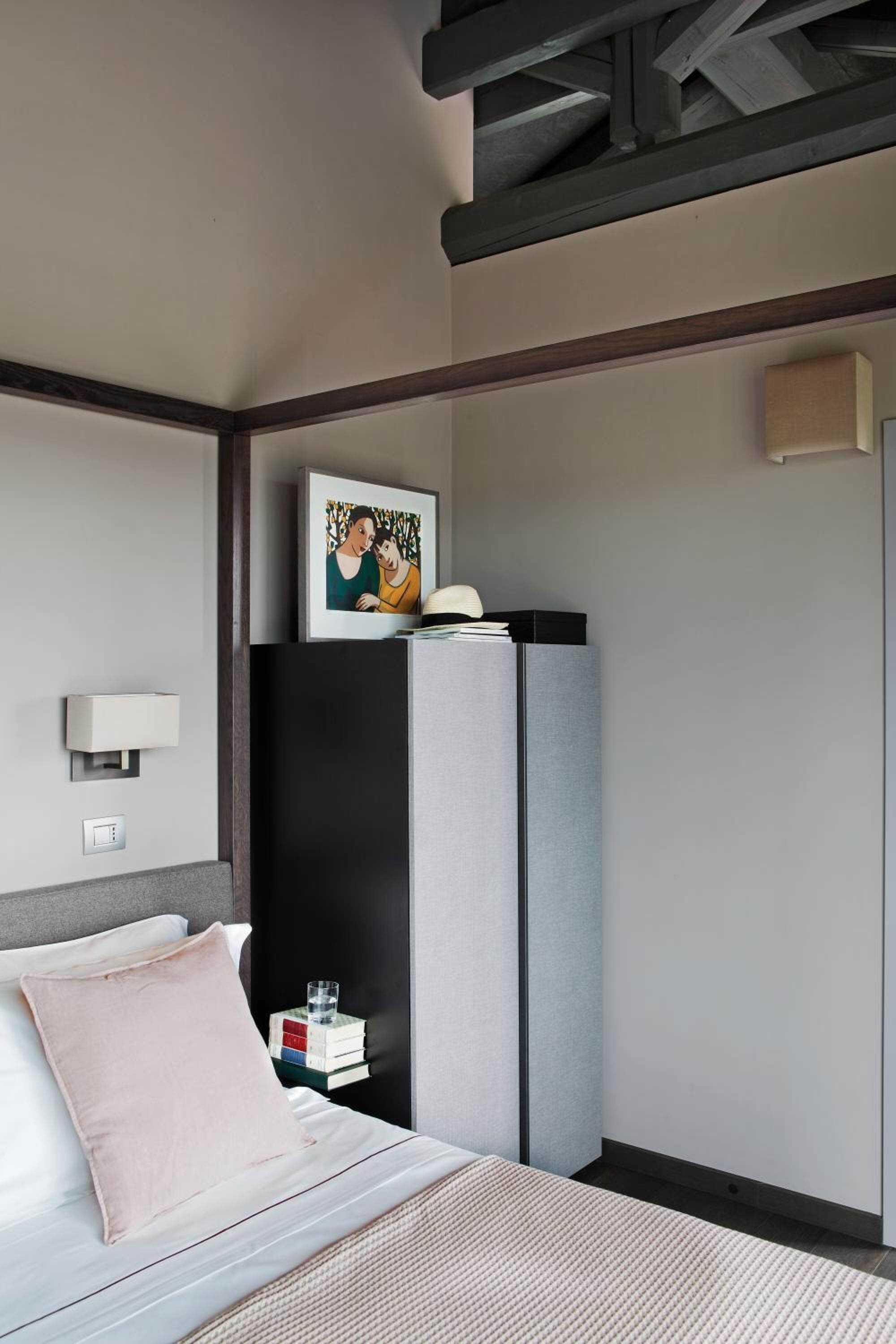 Una habitación de hotel moderna con una cama, una mesita de noche con lámpara, un armario y un cuadro en la pared.