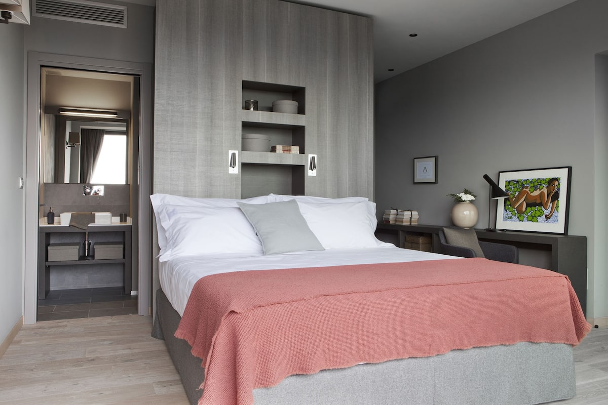 A modern bedroom with a large bed, grey walls, and built-in shelving.