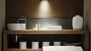 Un baño moderno con tocador de madera, lavamanos blanco y mesita de noche con toalla blanca.