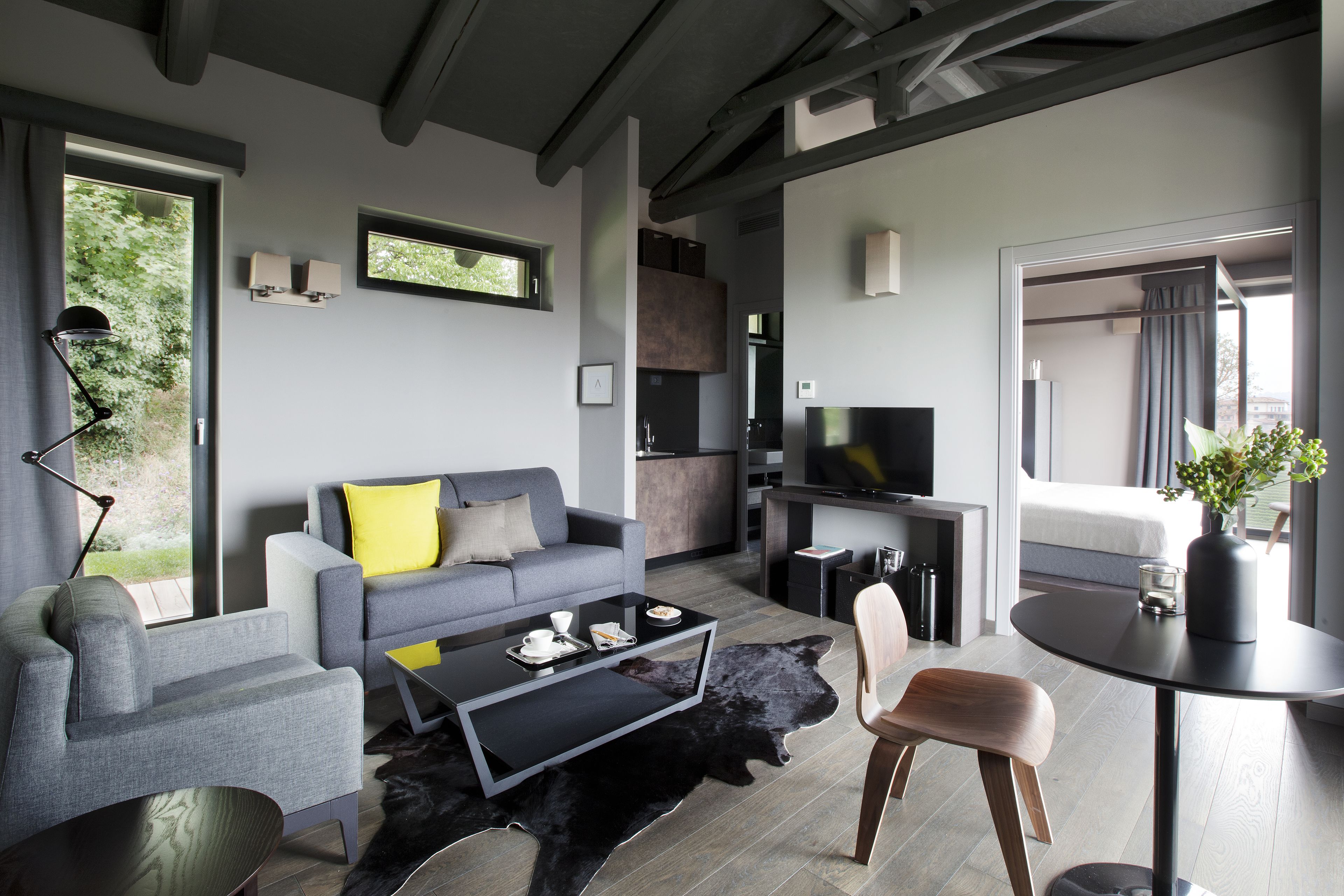 Una sala moderna con un sofá gris, una mesa de centro negra y un televisor. Hay un comedor con una mesa redonda y sillas.