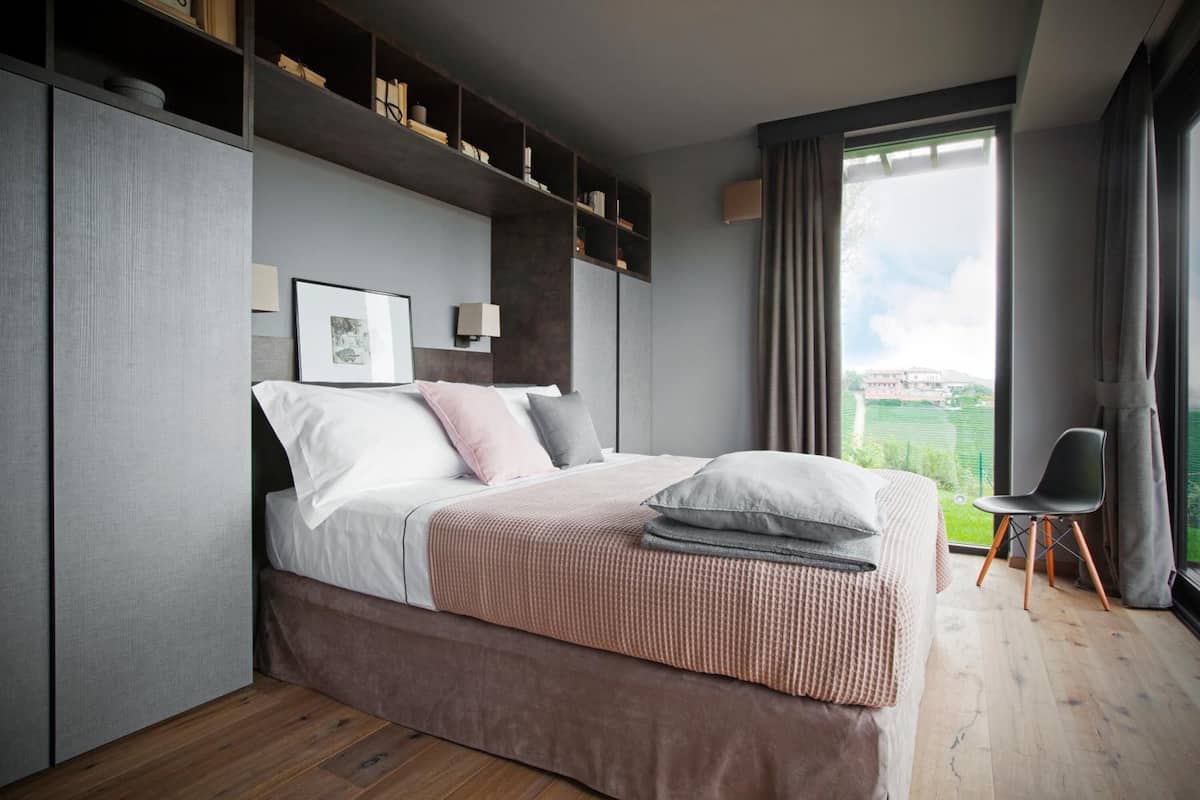 A modern bedroom with a large bed, built-in shelving, a desk, and a view of the outdoors.