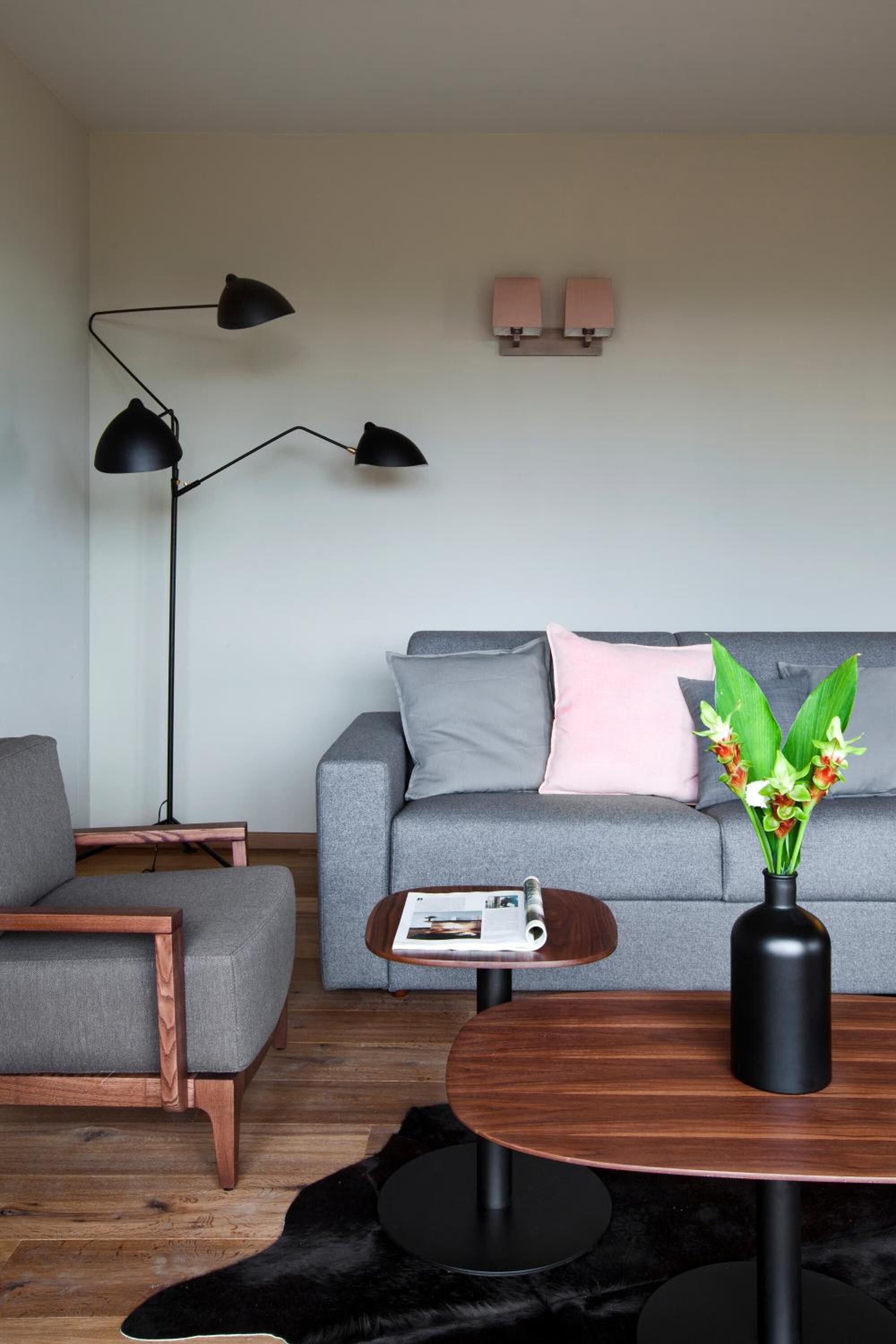 A modern living room with a grey sofa, a wooden coffee table, a black floor lamp, and a small side table with a magazine.