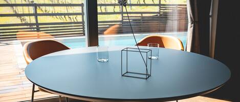 A round table with a metal base and four chairs, a glass on the table, and a view of a vineyard through large windows.