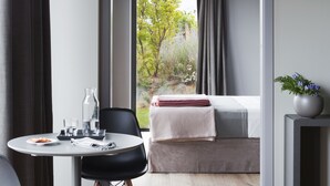 A modern room with a bed, a dining table with chairs, a small side table, and a view of greenery outside. - Arborina Relais (La Morra)