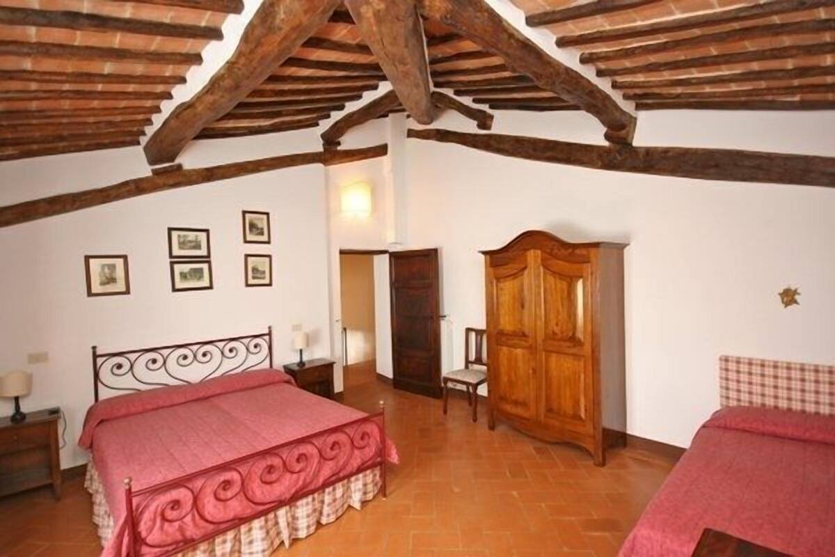 Quarto com teto de madeira, cama com colcha vermelha, guarda-roupa de madeira e uma cadeira.