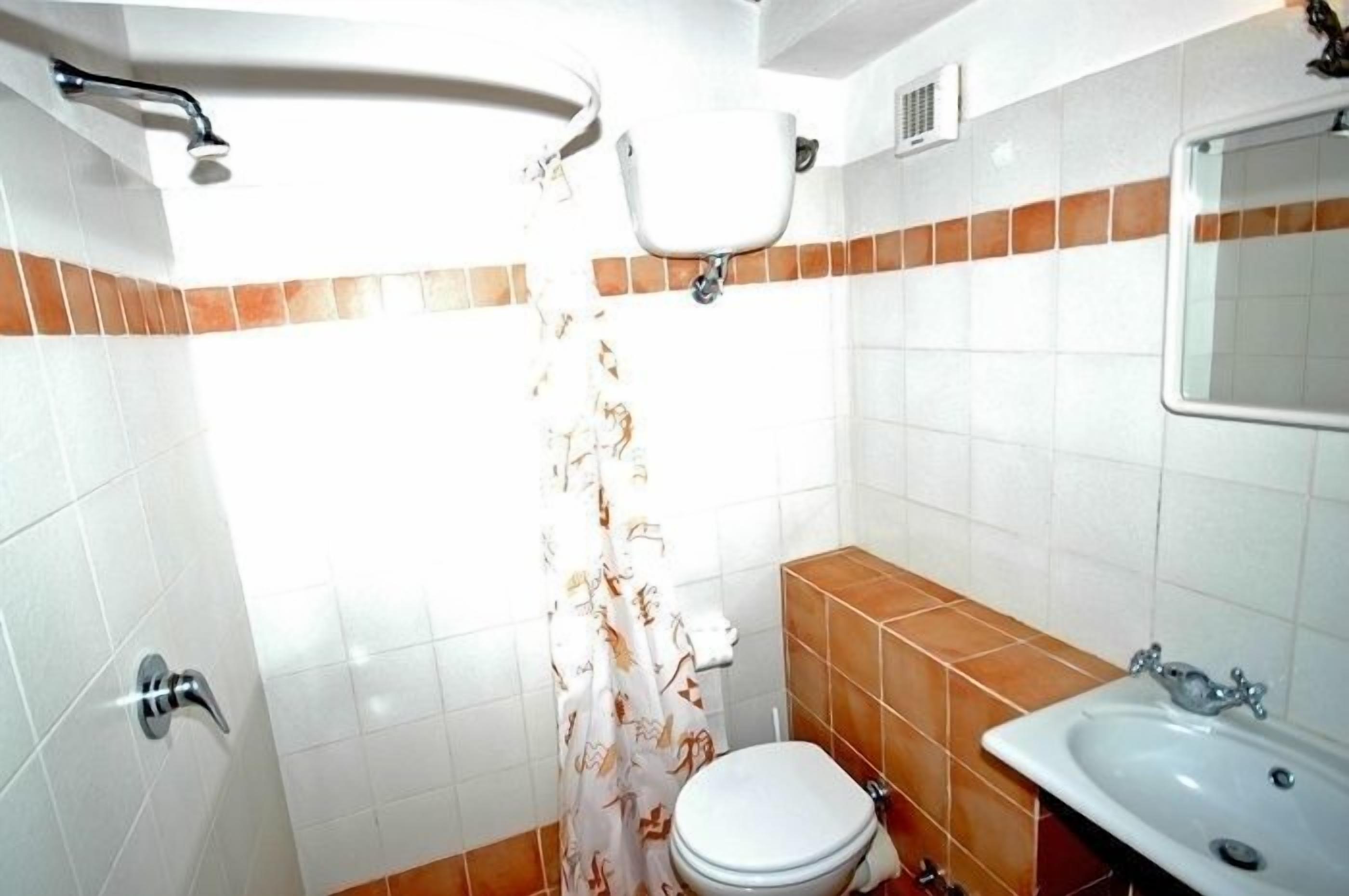 A bathroom with white and brown tiles, a toilet, a sink, and a shower with a curtain.