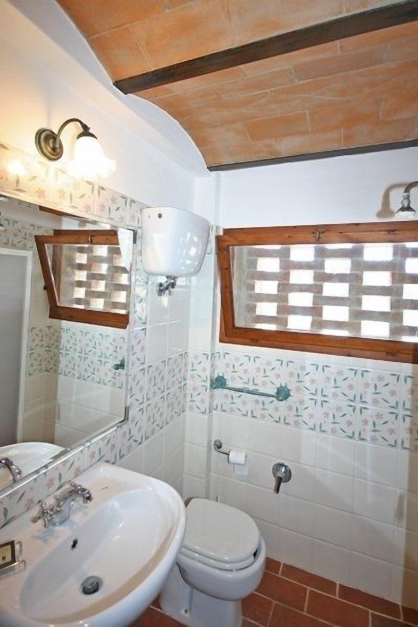 A bathroom with a white sink, a toilet, and a window with a wooden frame.