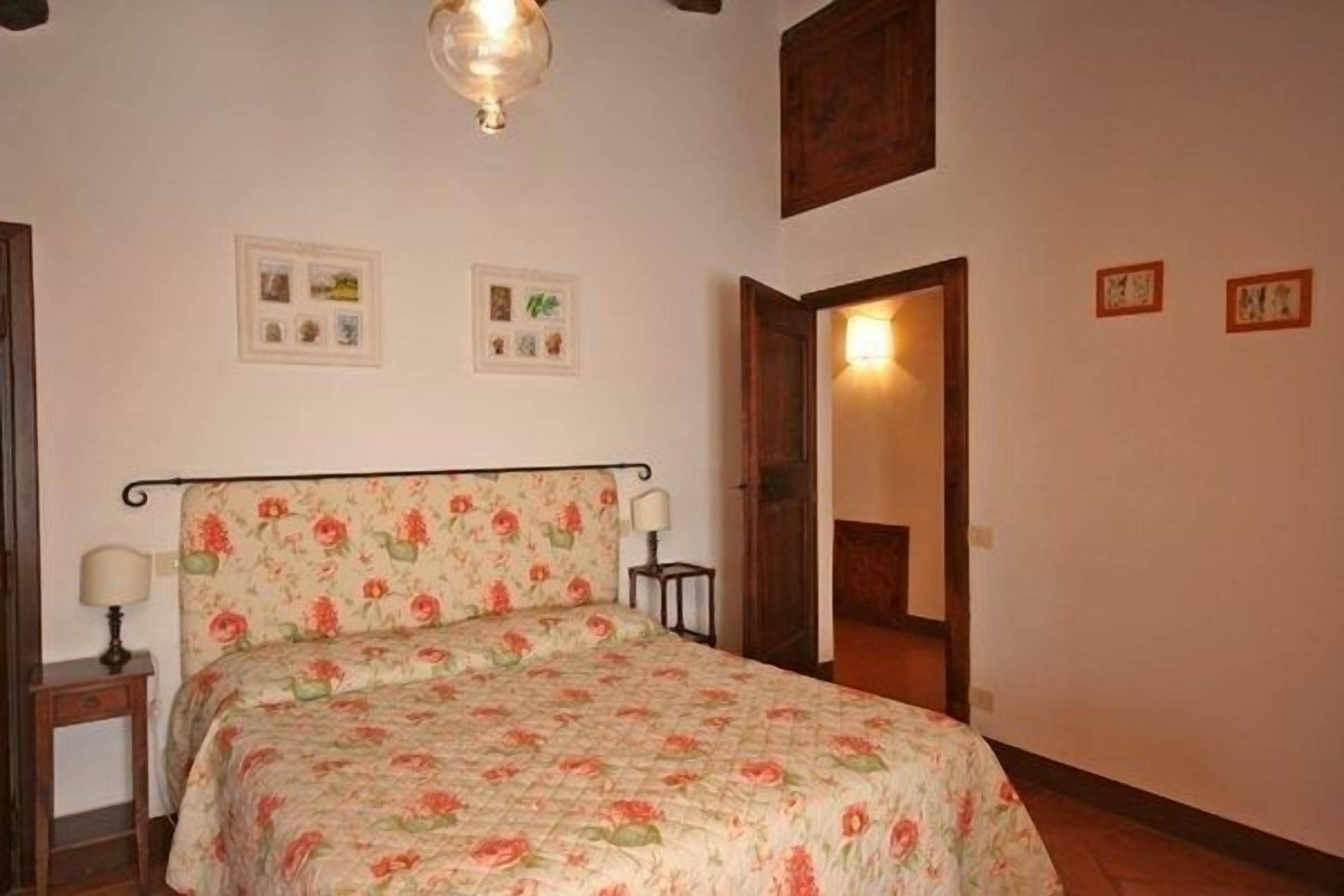 Ein Schlafzimmer mit Blumenmuster-Bettdecke, einem Nachttisch mit Lampe und einer Holztür zu einem anderen Raum.