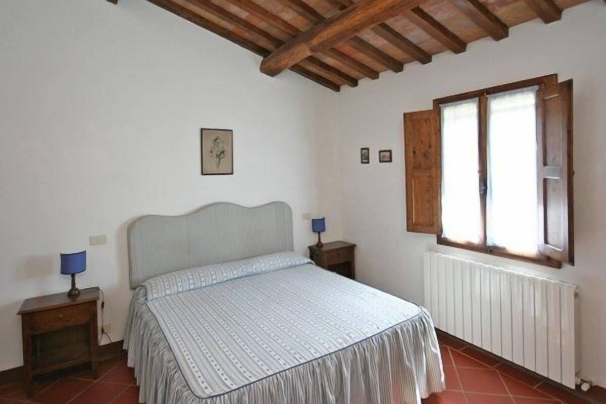 Um quarto com uma cama, duas mesas de cabeceira, uma janela com persianas de madeira e um radiador.