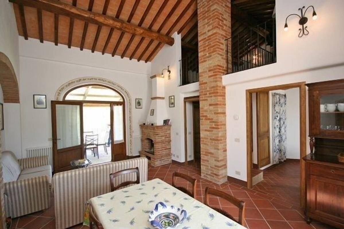 Um quarto espaçoso com teto alto, vigas de madeira aparentes, lareira e uma área de jantar com mesa e cadeiras.