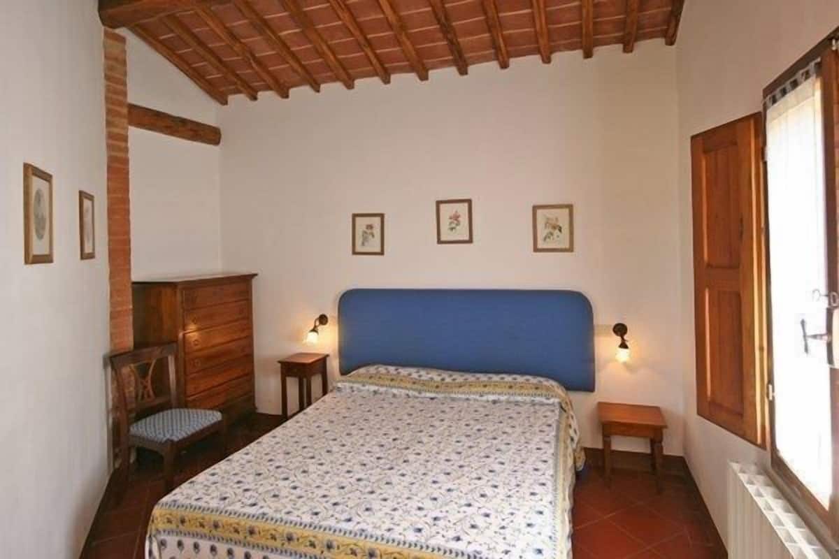 Quarto com cama, móveis de madeira, um banco e luminárias fixadas na parede.