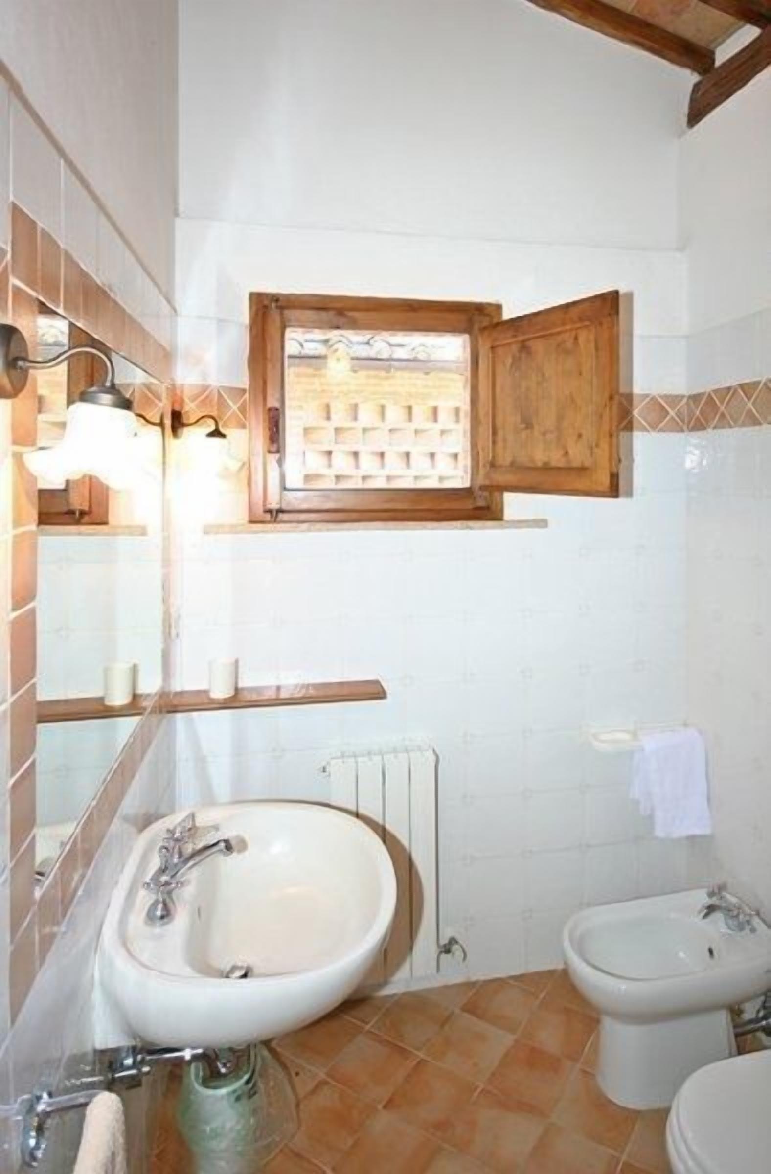 A bathroom with a sink, bidet, and a window with a wooden frame.