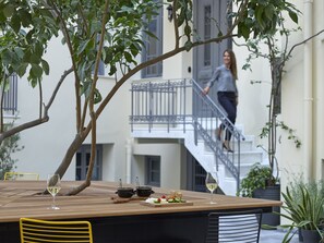 An outdoor dining area with a wooden table, two black pots, a glass of white wine, and a plate of vegetables. - innAthens (Athens)