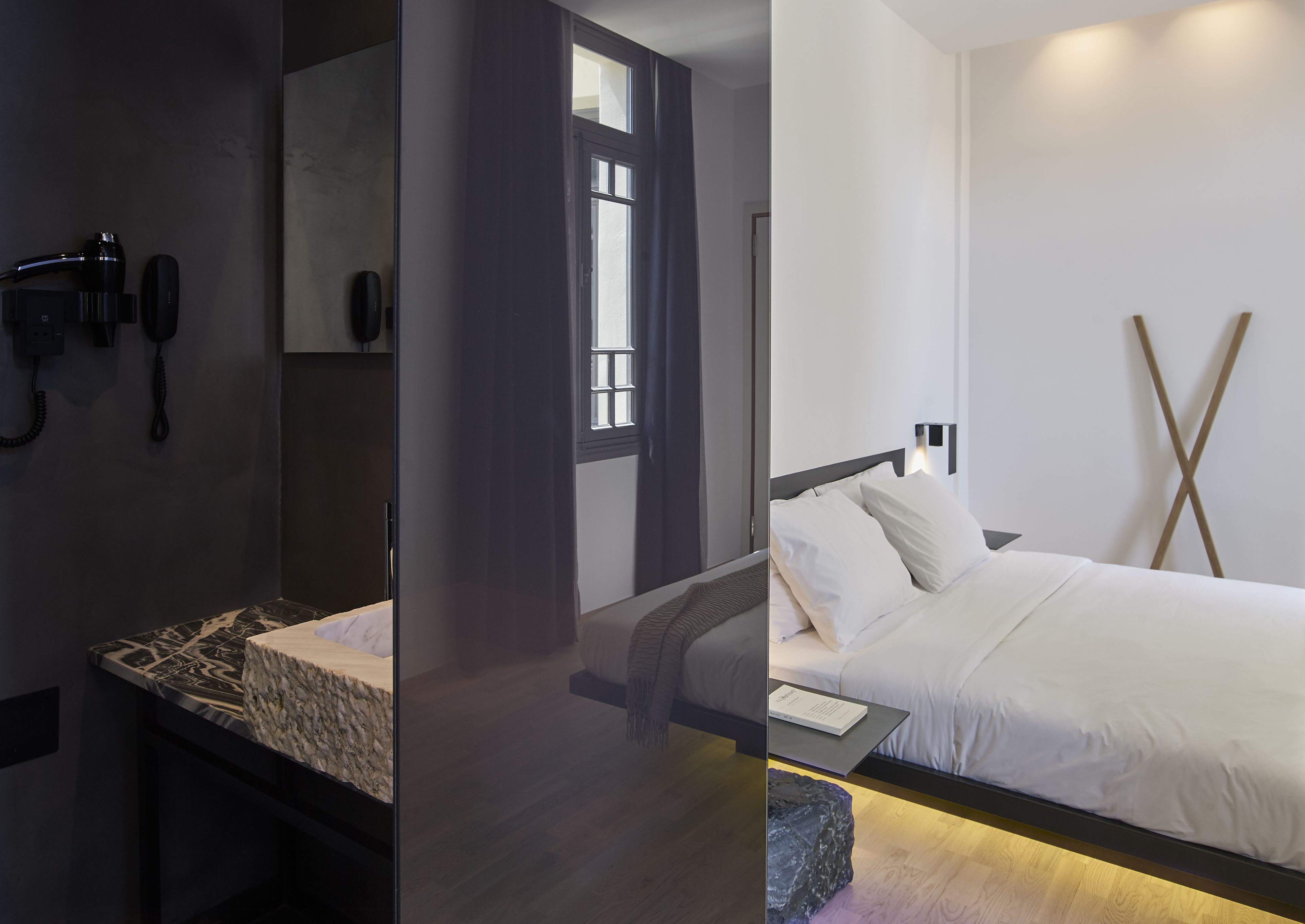 A modern hotel room with a bed, bedside table, and a phone on the wall.