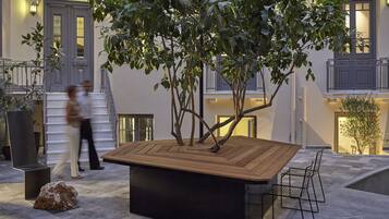 A courtyard with a wooden table and chairs, surrounded by potted plants and a stone floor.