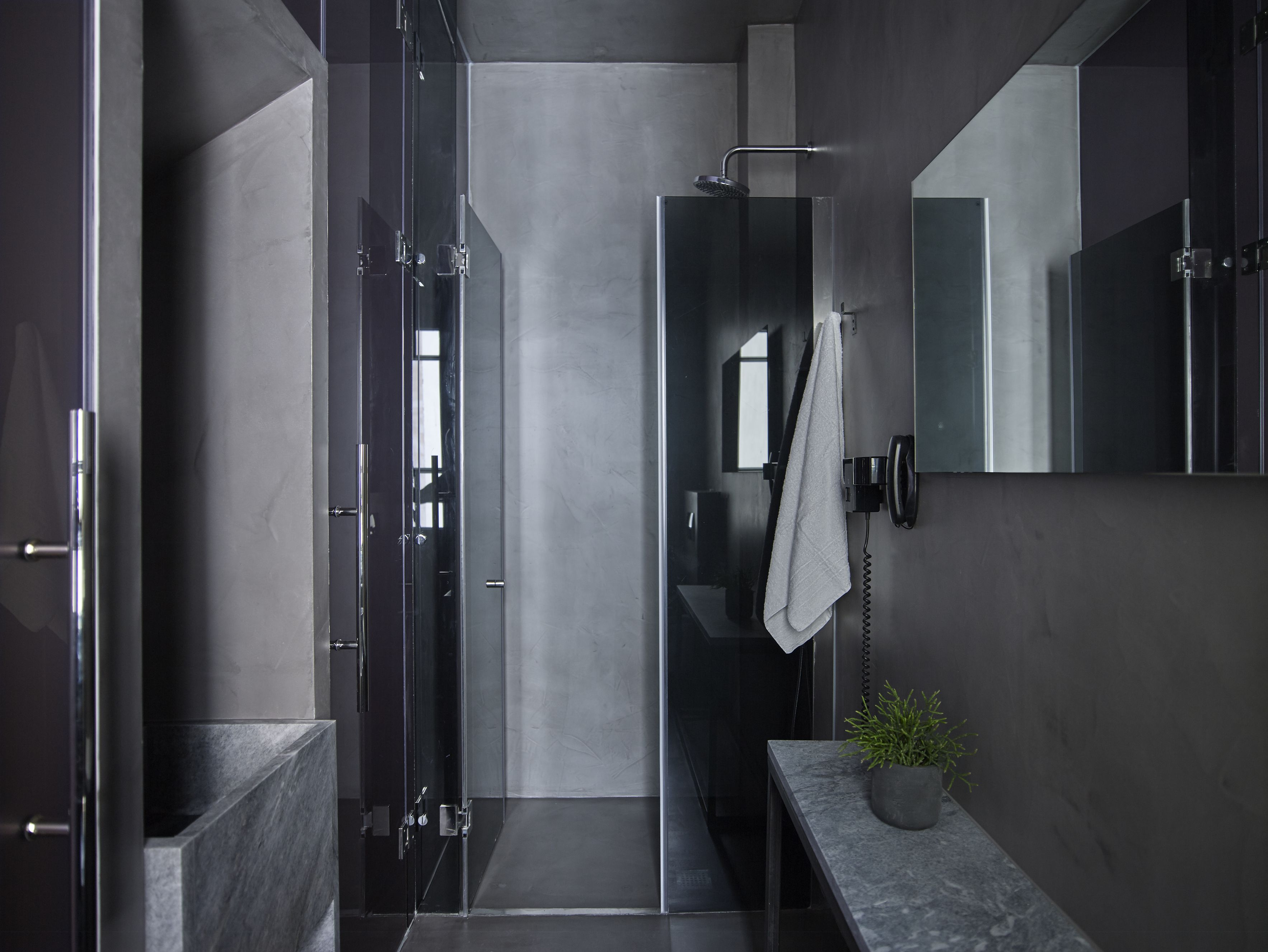A modern bathroom with a glass shower enclosure, a marble countertop, and a potted plant.