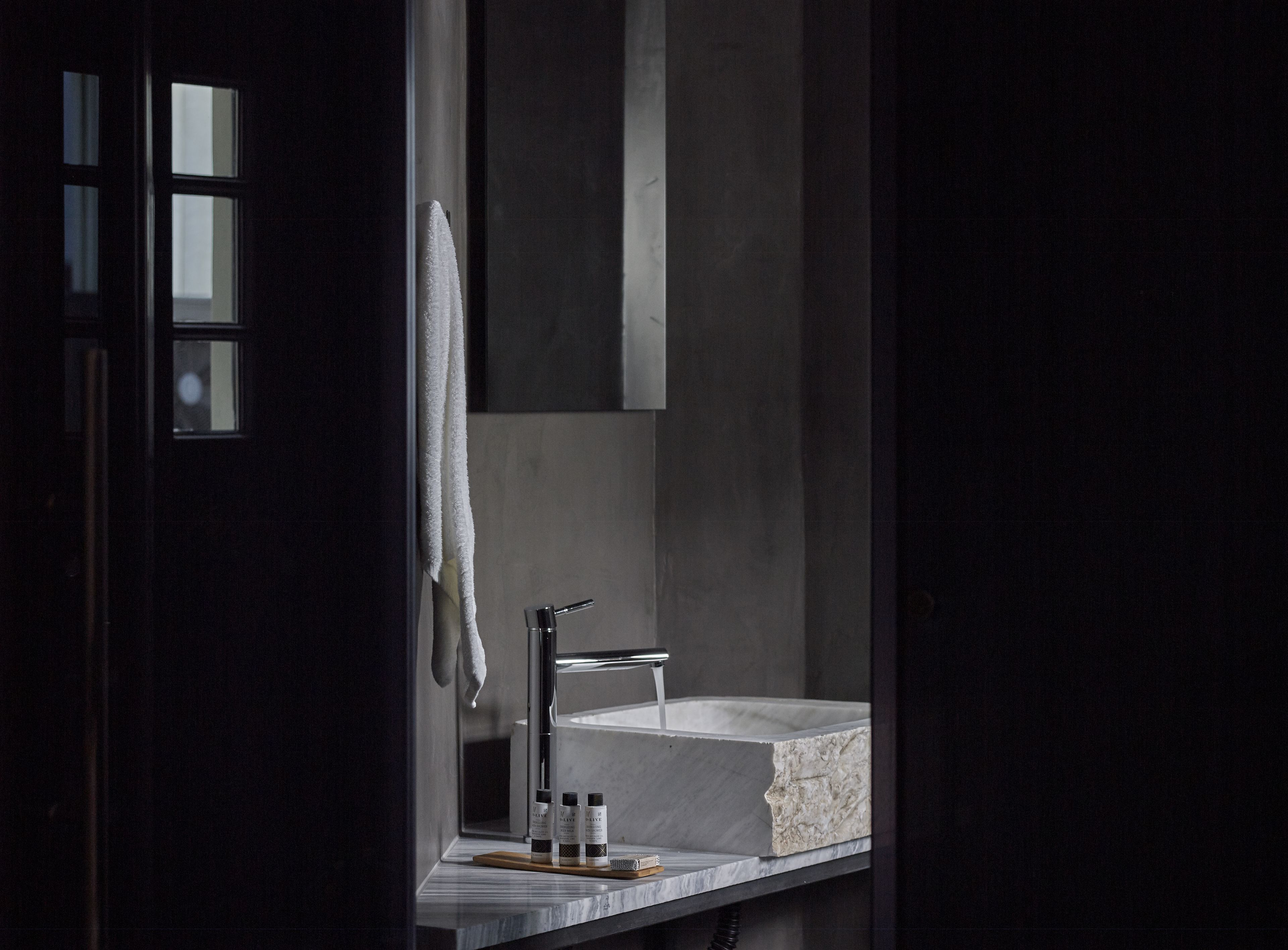 Ein modernes Badezimmer mit einem Marmorwaschbecken, einem Handtuch an der Wand und Toilettenartikeln auf der Ablagefläche.