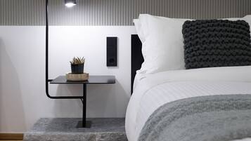 A modern bedroom with a bed, bedside table, lamp, and a small potted plant.