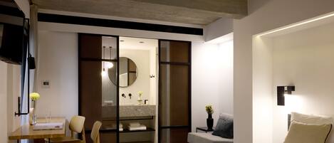 A modern hotel room with a large bed, a desk with a chair, a vanity with a mirror, and a sliding door closet.