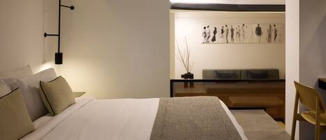 A modern hotel room with a large bed, a bedside table, a chair, and a wall-mounted artwork.