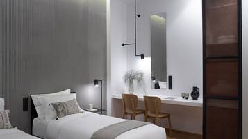 A modern hotel room with a large bed, a desk with a chair, a mirror, and a potted plant.